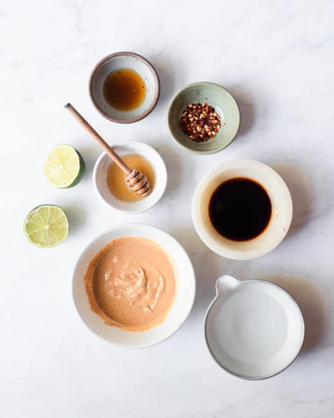 all of the ingredients for peanut dressing in different sized bowls and plates on a marble surface