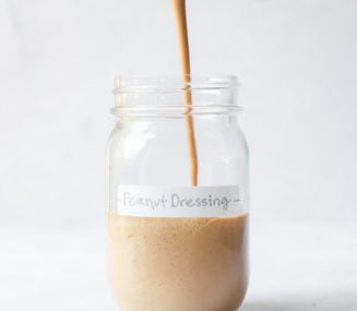 a person pouring peanut dressing into a labeled mason jar