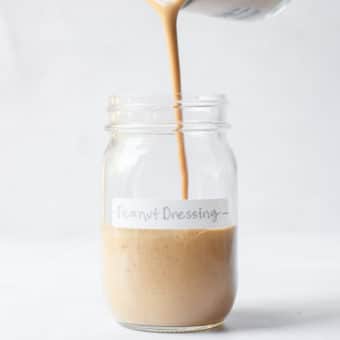 a person pouring peanut dressing into a labeled mason jar