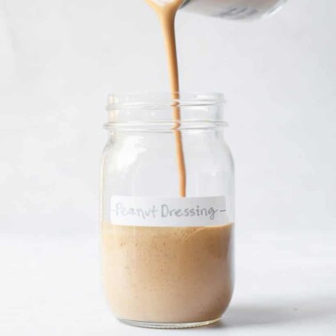 a person pouring peanut dressing into a labeled mason jar