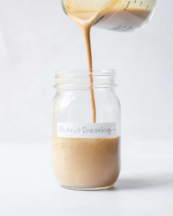 a person pouring peanut dressing into a labeled mason jar