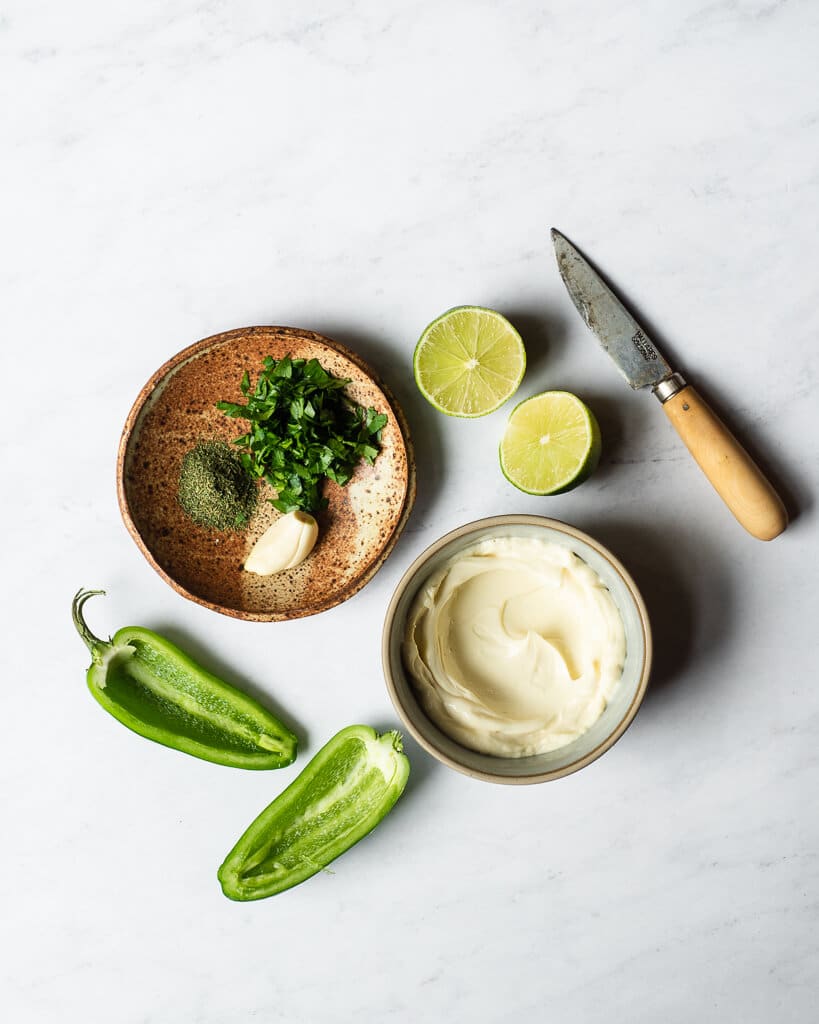 all of the ingredients for a homemade jalapeno ranch dressing in different sized bowls and plates on a marble surface