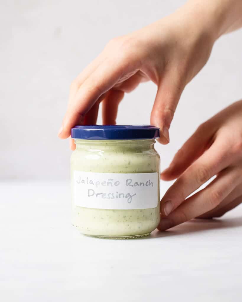 a person's hands on a small labeled jar of jalapeno ranch dressing