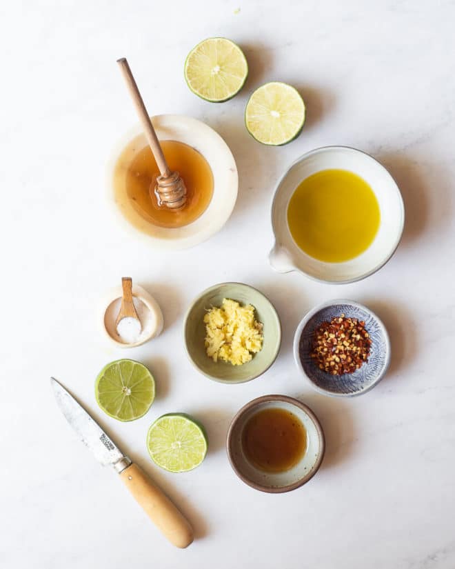 all of the ingredients for homemade sesame lime dressing in different sized bowls and plates on a marble surface