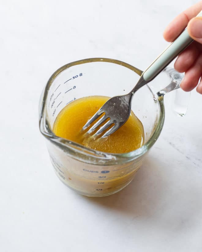 a person whisking together the ingredients for sesame lime dressing using a fork