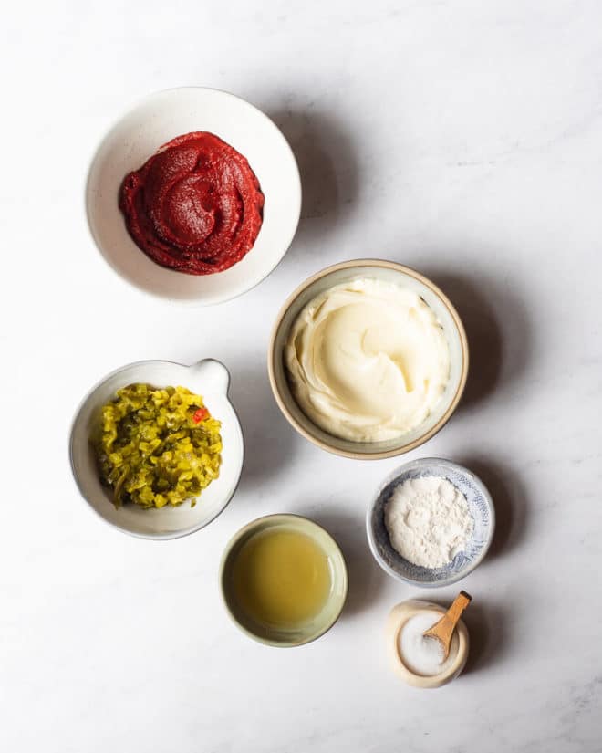 all of the ingredients for homemade thousand island dressing in different sized bowls on a marble surface