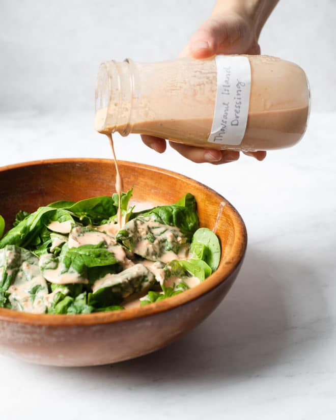 a wooden bowl of spinach being drizzled with homemade thousand island dressing