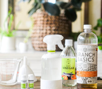 the ingredients for all purpose cleaner: branch basics concentrate, essential oils, and white vinegar sitting on a kitchen table