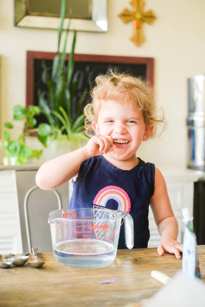 a little girl sitting at the table with a large measuring cup of safe, non toxic all purpose cleaner in front of her