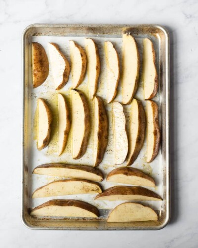 potato wedges coated in olive oil, salt, and pepper lined up on a sheet pan