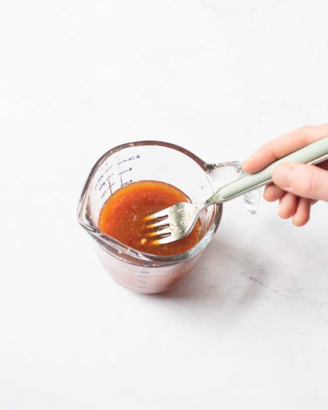 a person using a fork to whisk together a homemade thai salad dressing