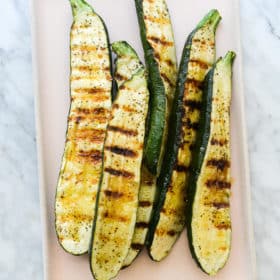 5 grilled zucchini halves on a pink rectangular plate