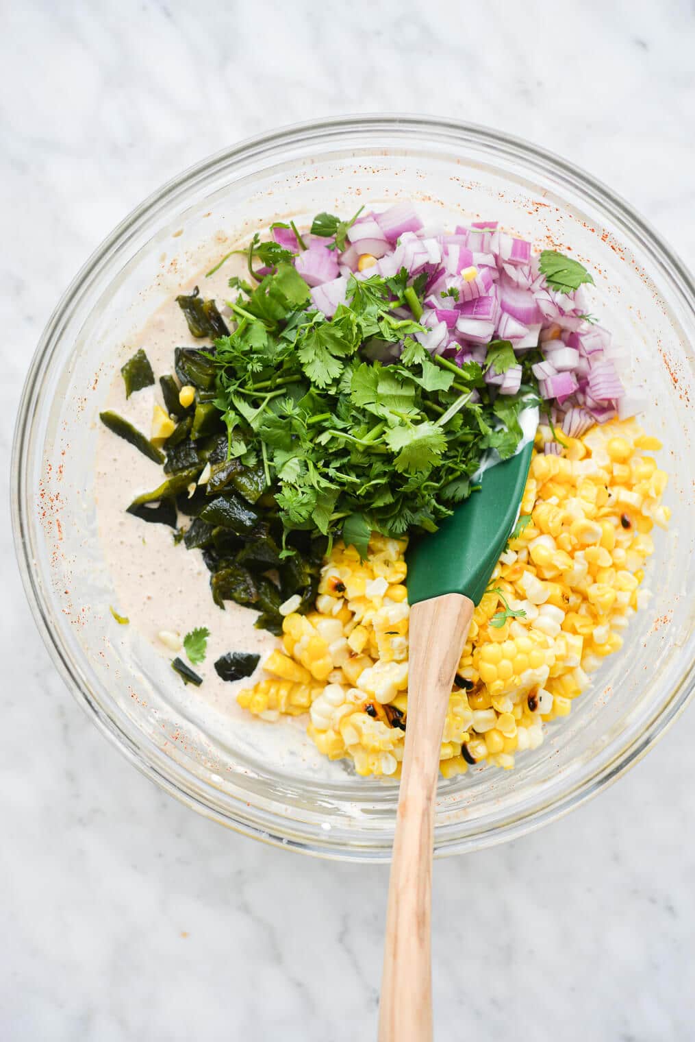 the ingredients for a mexican street corn salad in a large bowl being mixed together with a rubber spatula