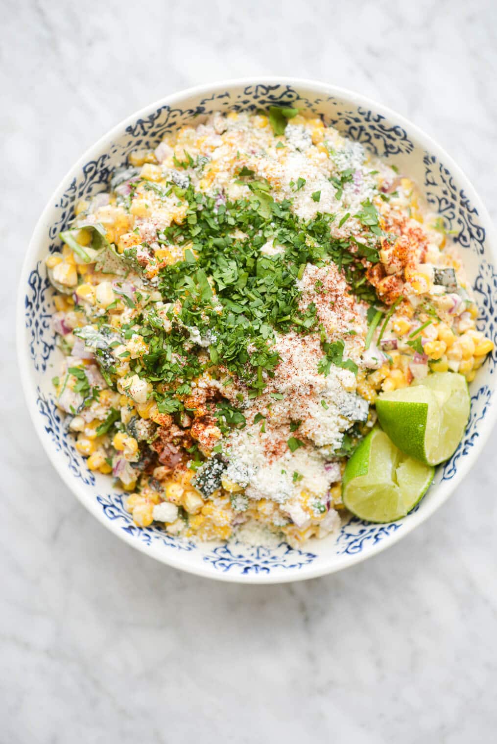 a bowl of mexican street corn salad garnished with cotija cheese, cilantro, lime wedges, and tajin