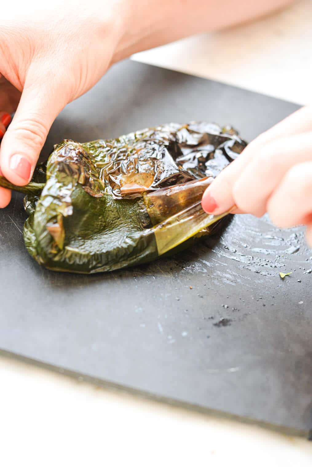 a person peeling the skin off of grilled poblano peppers