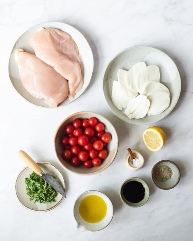 the ingredients for caprese chicken skillet in different sized bowls and plates on a marble surface