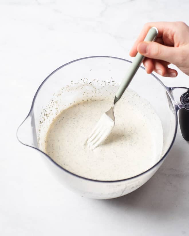 a person using a fork to whisk together a homemade ranch dressing in a large, spouted, glass measuring cup