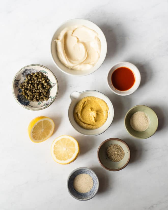 the ingredients for a homemade remoulade sauce in different sized bowls on a marble surface