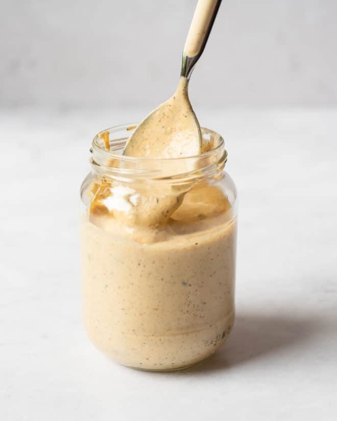 a person using a spoon to scoop out homemade remoulade sauce from a glass jar
