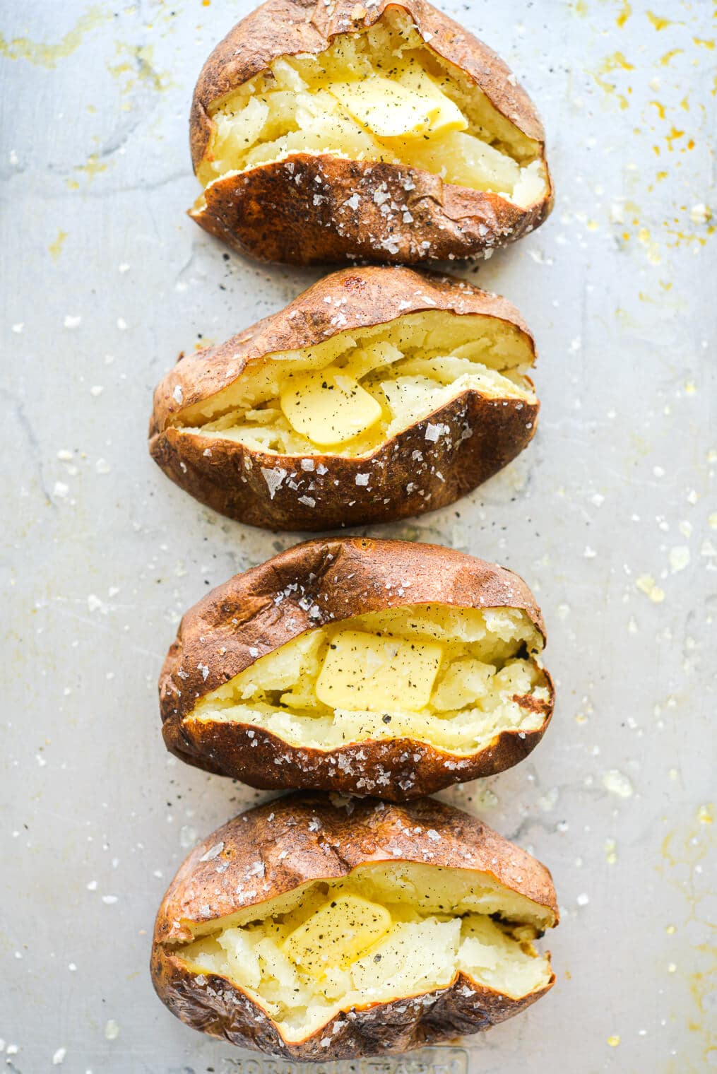 4 cooked and split open baked potatoes on a metal sheet pan