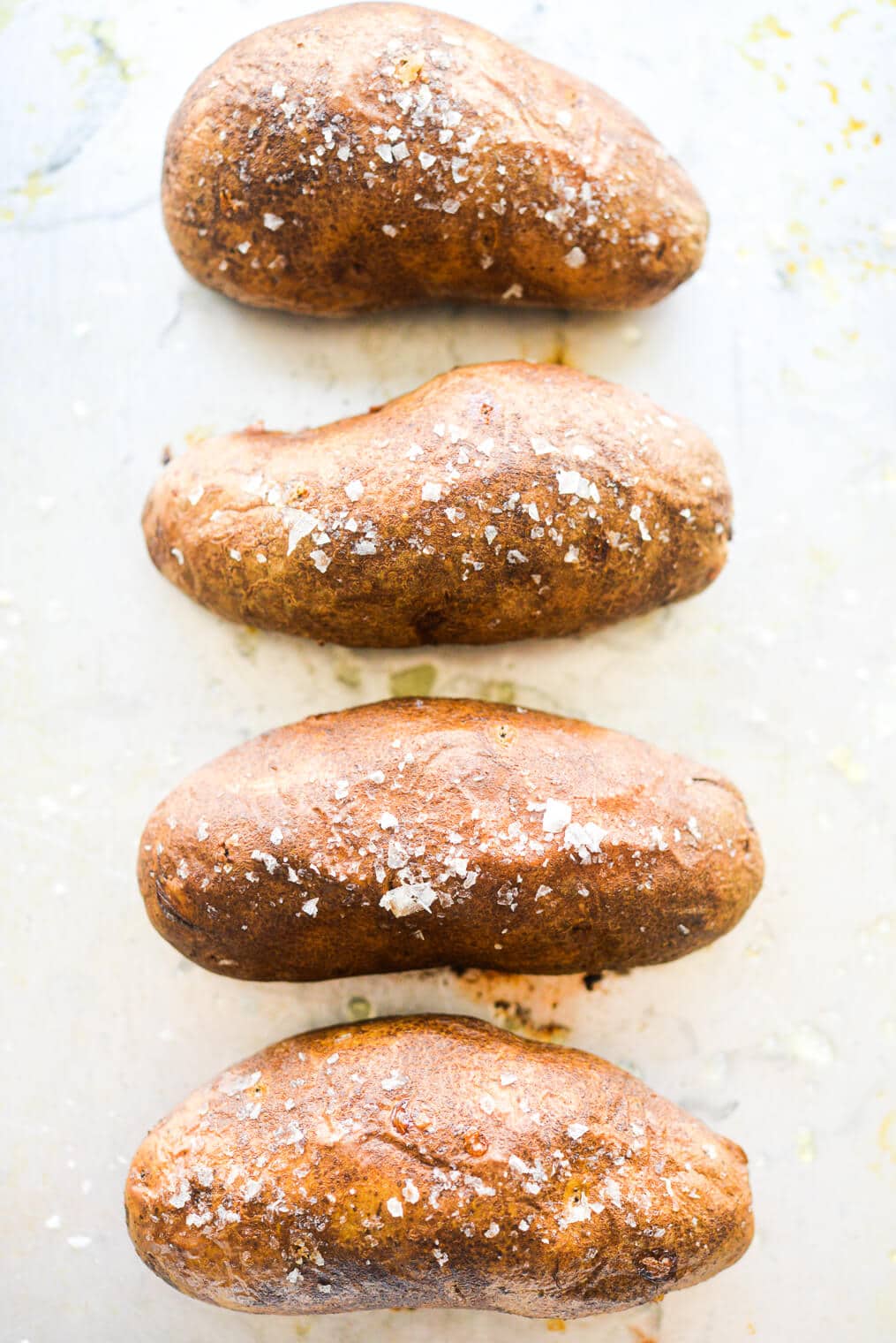 4 salted baked russet potatoes on a metal sheet pan