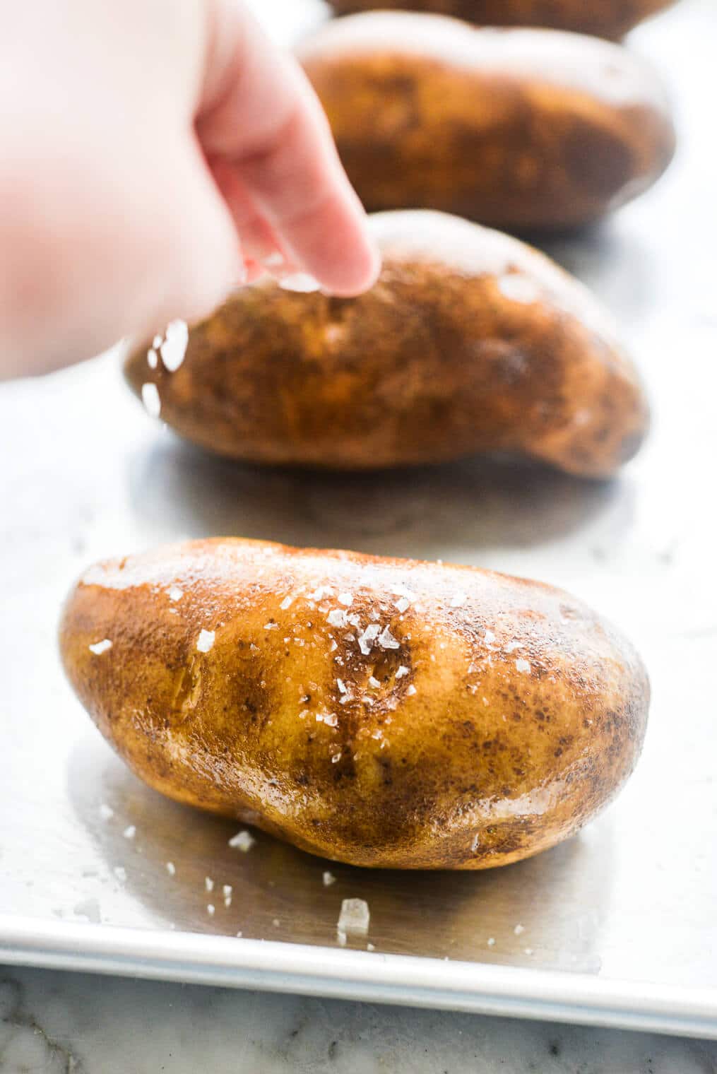 someone salting olive oil rubbed raw russet potatoes