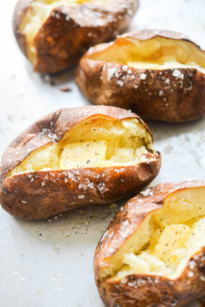 4 split open baked potatoes on a metal sheet pan