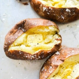 4 split open baked potatoes with butter, salt, and pepper in each of them