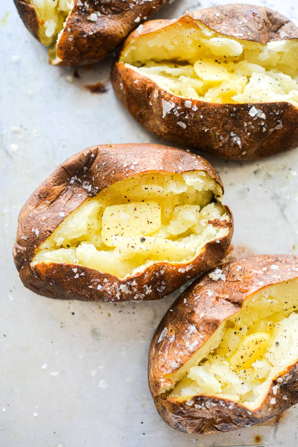 4 split open baked potatoes with butter, salt, and pepper in each of them