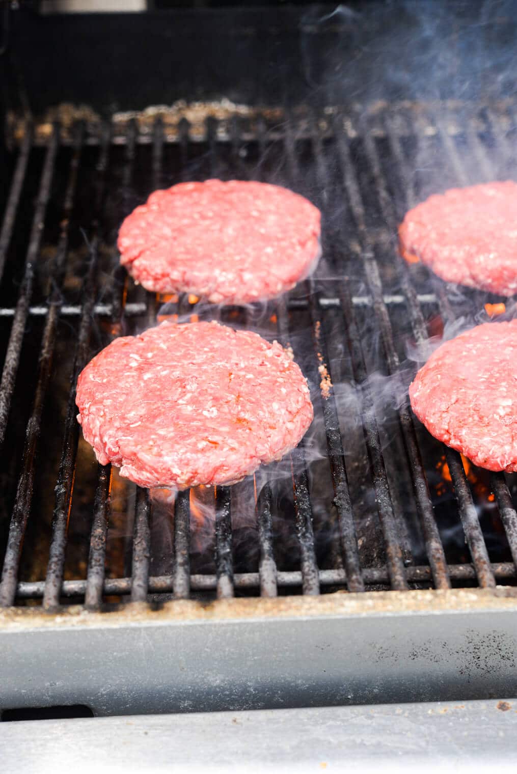 4 ground beef patties on the grill grates of a gas grill