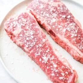 two steaks that have been heavily salted sitting on a plate