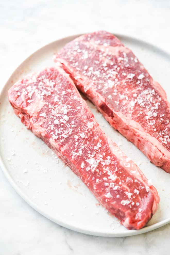 two steaks that have been heavily salted sitting on a plate