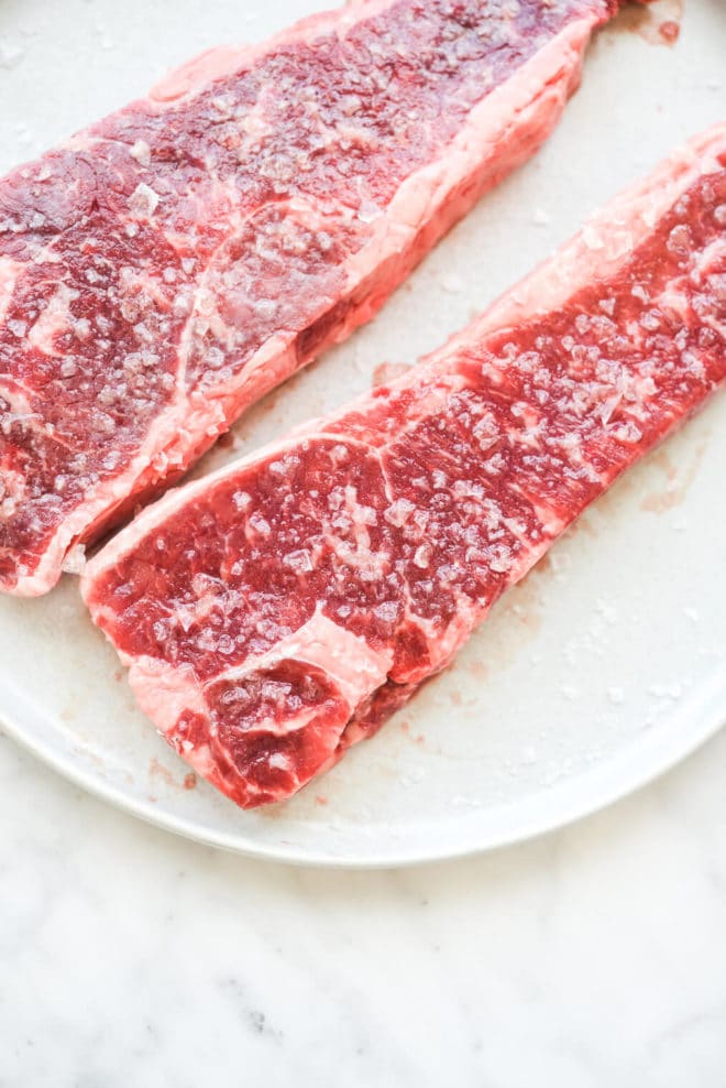 two steaks that have been heavily salted sitting on a plate