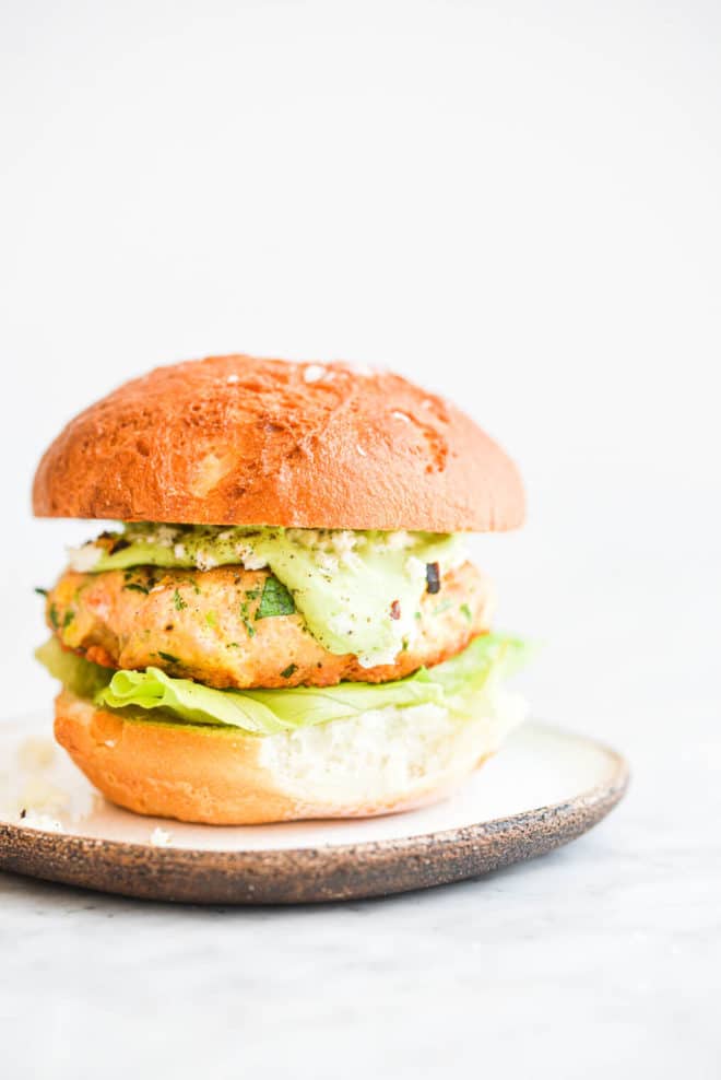 a salmon burger on a bun with lettuce and green goddess dressing