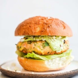 a salmon burger on a bun with lettuce and green goddess dressing