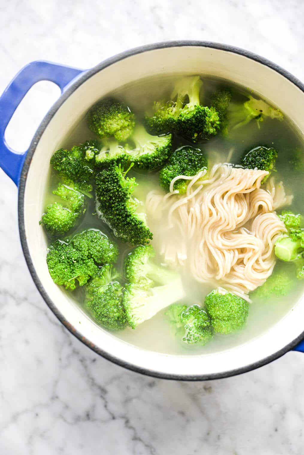 an enameled cast iron pot of water with broccoli and ramen noodles boiled in them