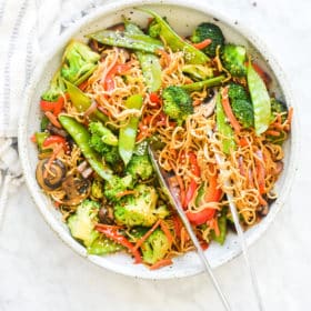 a large bowl of finished veggie noodle stir fry with tongs in the bowl
