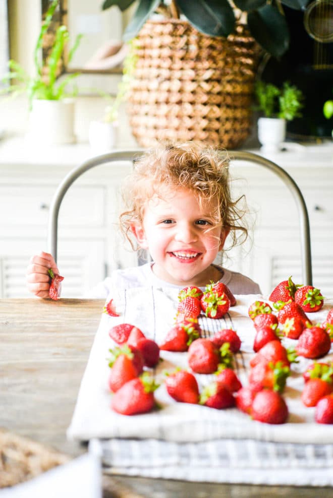 a little girl sitting down at a table and smiling behind a bunch of strawberries spread out on a kitchen towel