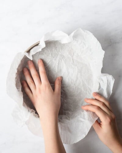 a person placing parchment paper in a circular baking dish