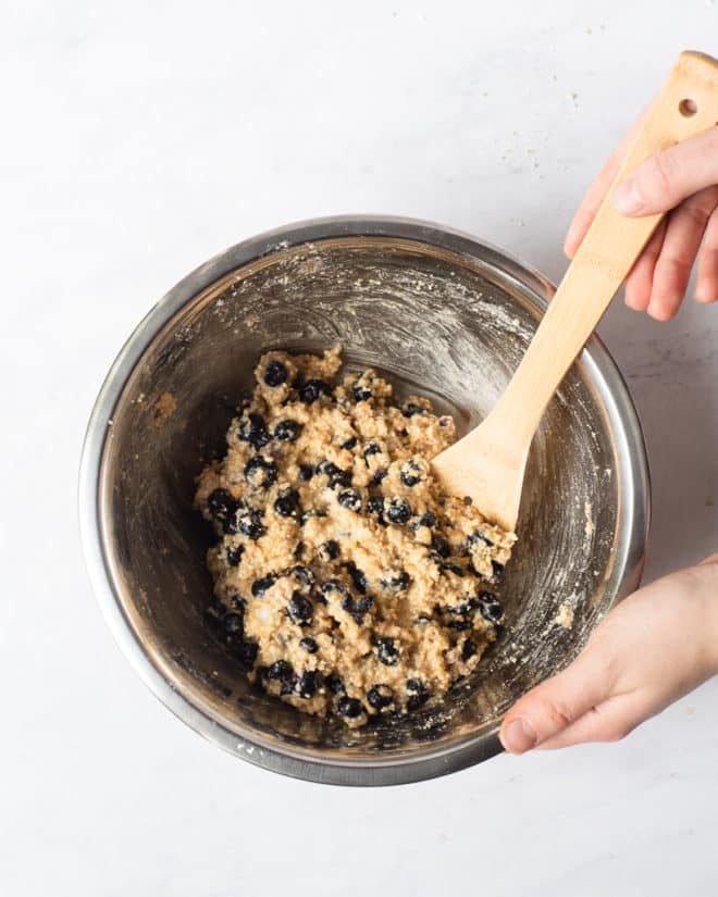 blueberry scone batter being stirred up in a metal mixing bowl with a wooden spoon