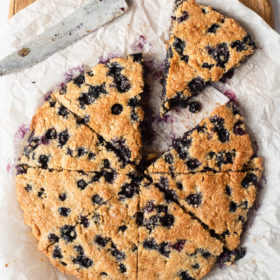 a batch of blueberry scones cut into slices sitting on a parchment paper lined cutting board next to a knife