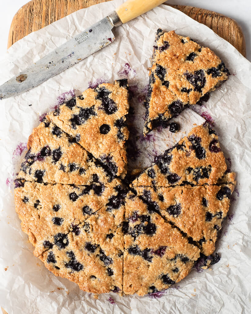 a batch of blueberry scones cut into slices sitting on a parchment paper lined cutting board next to a knife