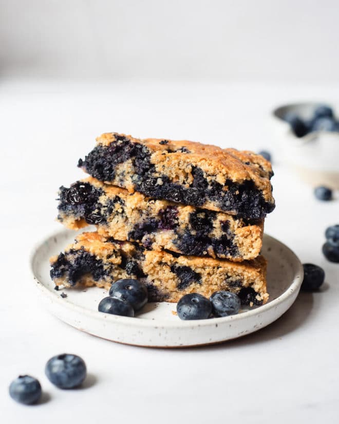 a small plate with three blueberry scones stacked on top of one another next to several fresh blueberries