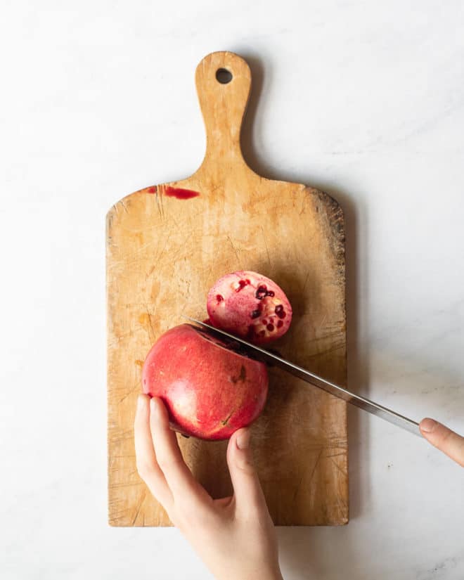 a person cutting the top off of a pomegranate on a large wooden cutting board