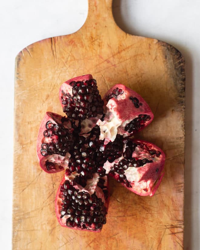 a segmented pomegranate sitting on a wooden cutting board