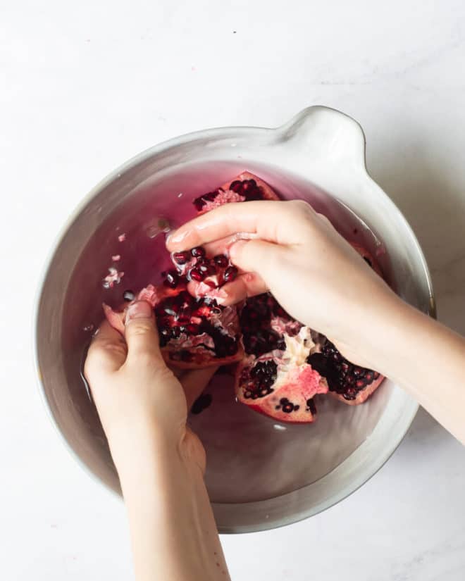 a person getting the seeds out of a pomegranate using their hands in a large bowl of water