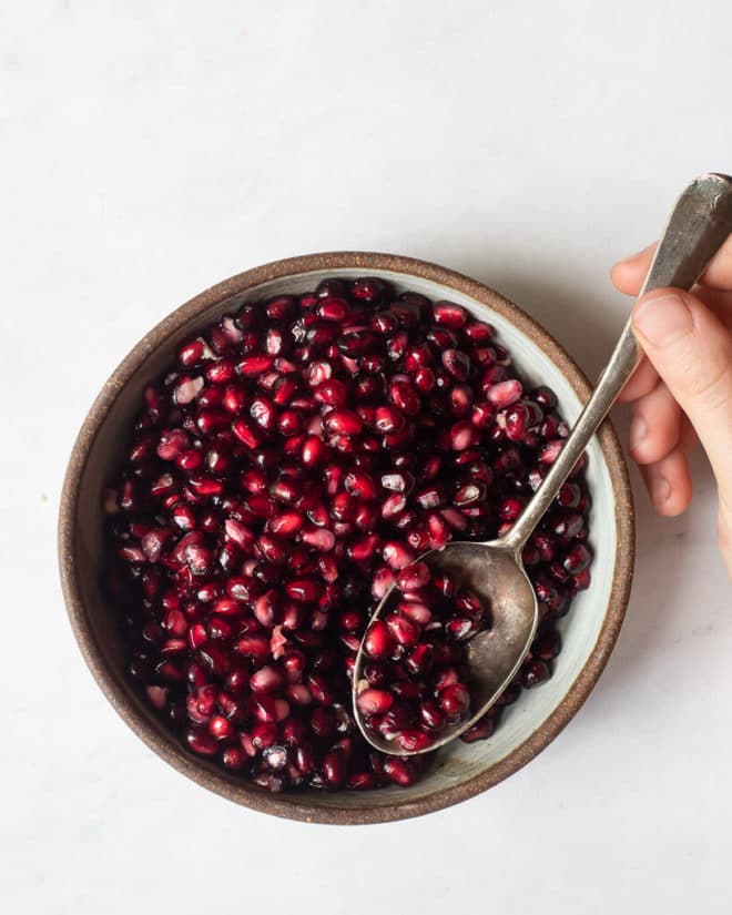 a bowl of pomegranate seeds with a person spooning out some of them