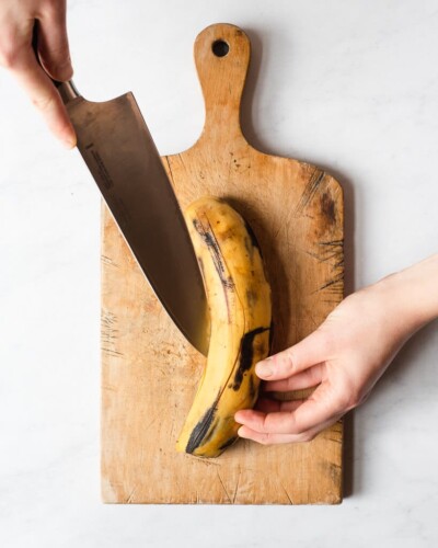 a person scoring the peel of a plantain with a large knife