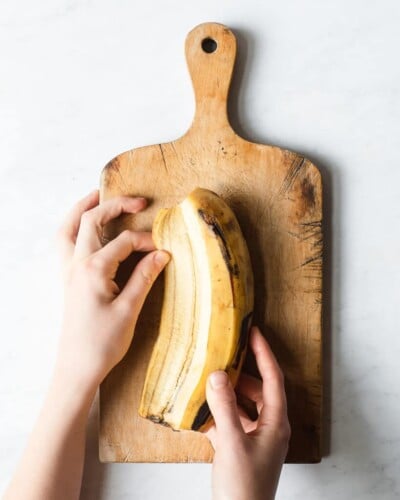 a person peeling a plantain on a wooden cutting board