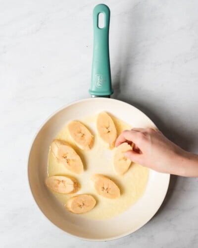 someone pan frying sliced plantains in a ceramic pan